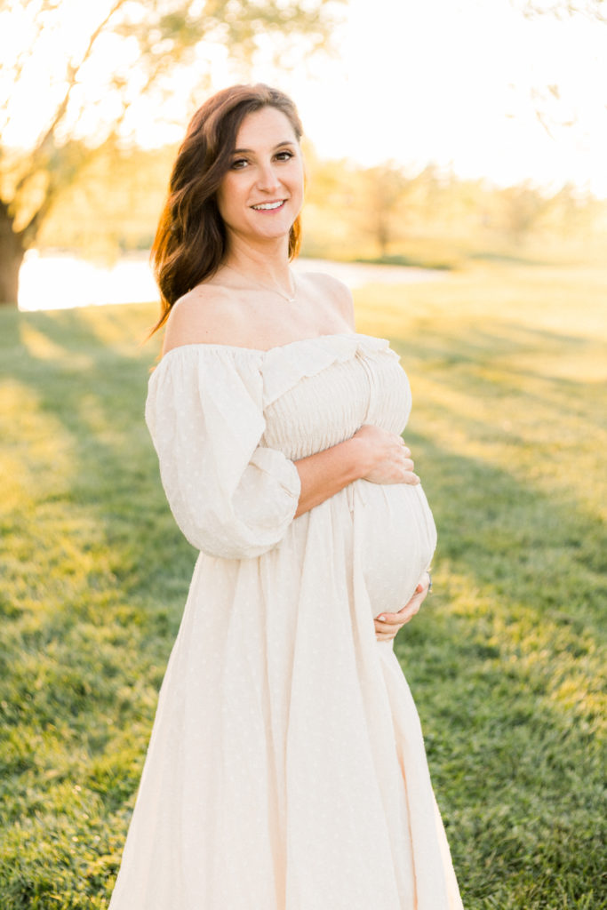 7 months pregnant woman smiles in light of the sunset at maternity session at coxhall gardens in carmel indiana