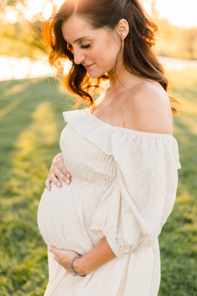 7 months pregnant woman glowing in light of the sunset at maternity session at coxhall gardens in carmel indiana