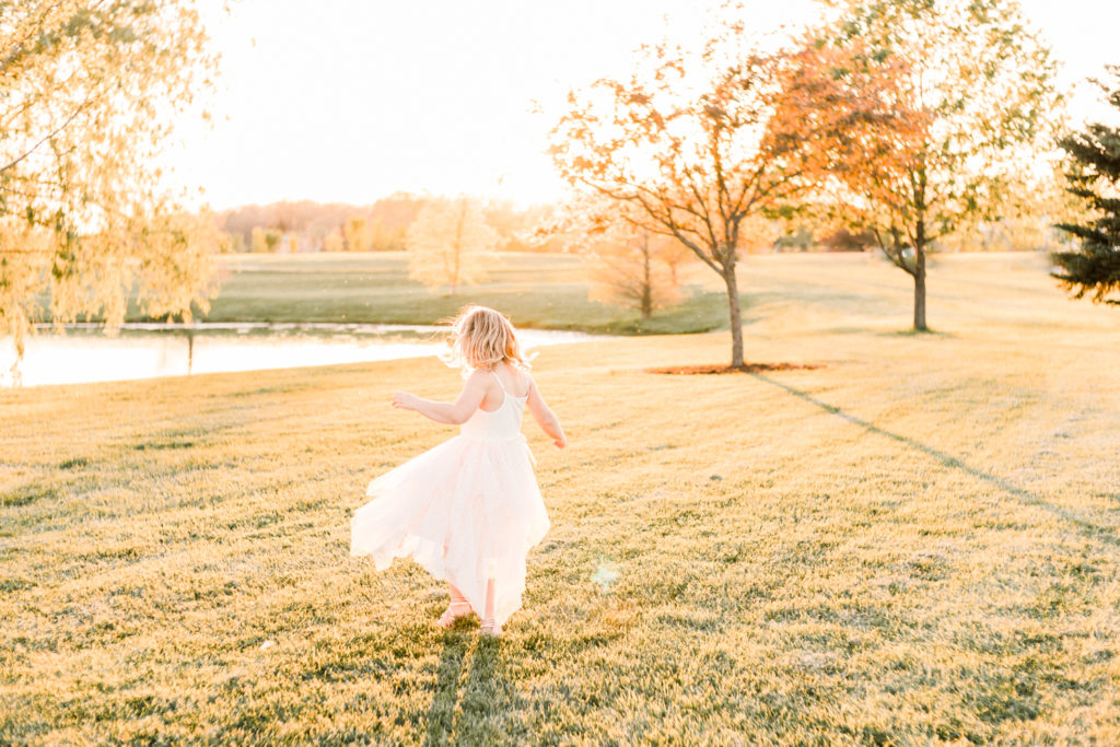young girl twirls by pond in light of the sunset at maternity session at coxhall gardens in carmel indiana