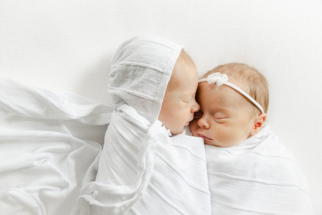 Newborn twins swaddled in white laying on a white blanket facing each other Carmel newborn photographer