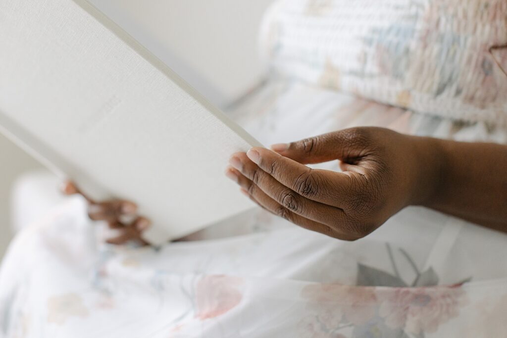 Close up of a woman in a floral dress flips through a grey linen covered heirloom album of Carmel family pictures.