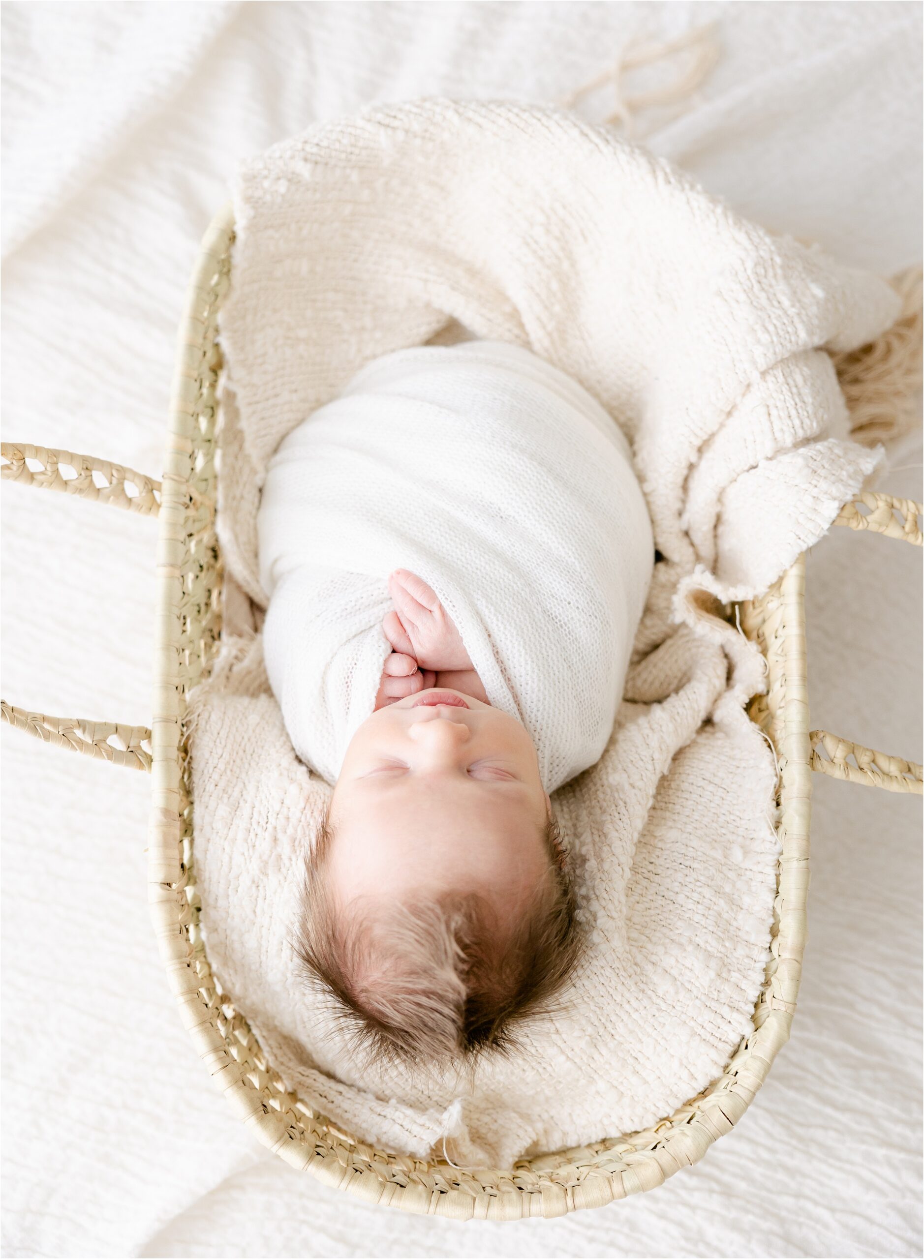 newborn baby swaddled in white blanket lying in a moses basket, how much to invest on newborn & family photography