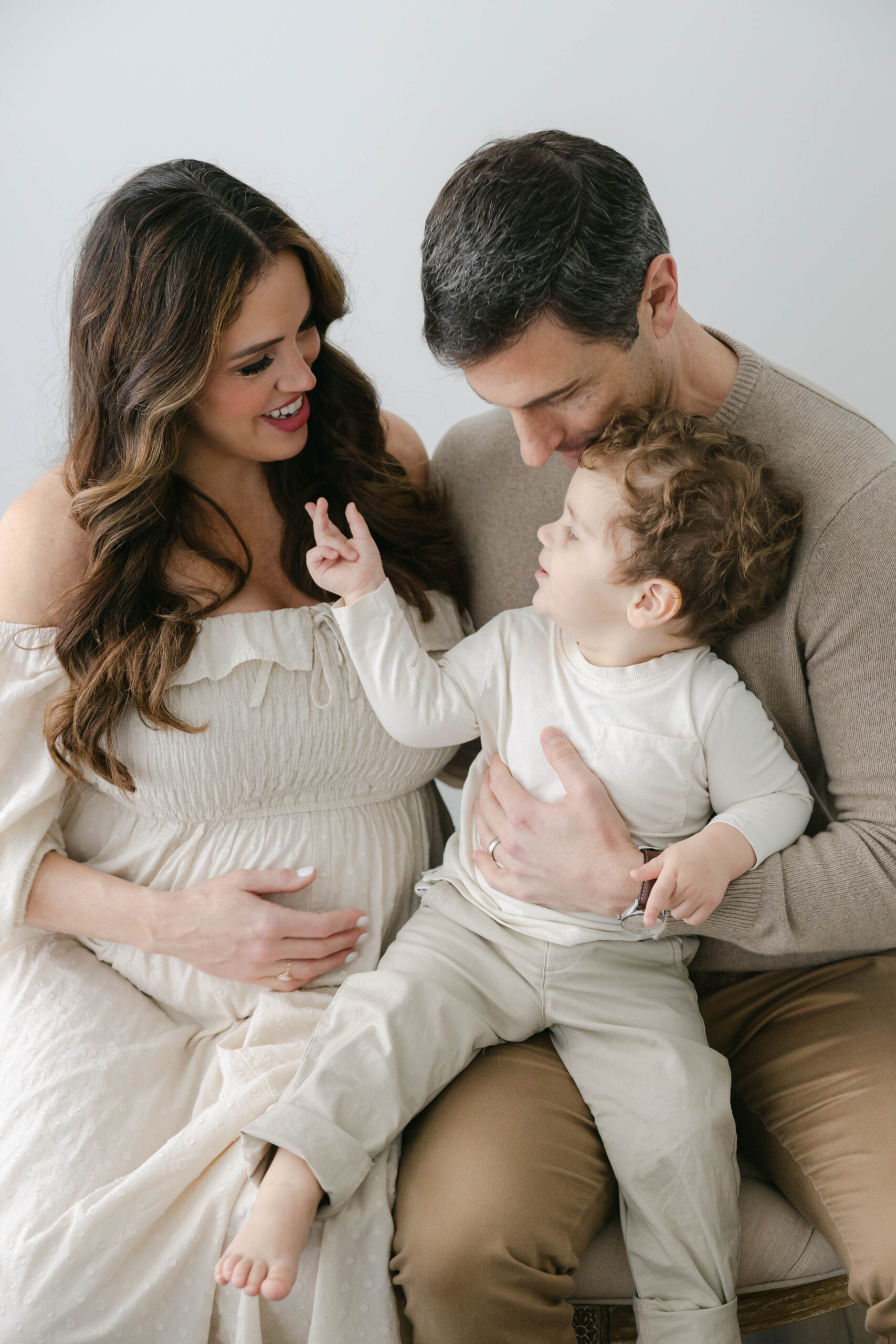 mother and father looking at their toddler as he reaches up to his mother while dressed in creams and browns, Session styling tips, Zionsville maternity photographer
