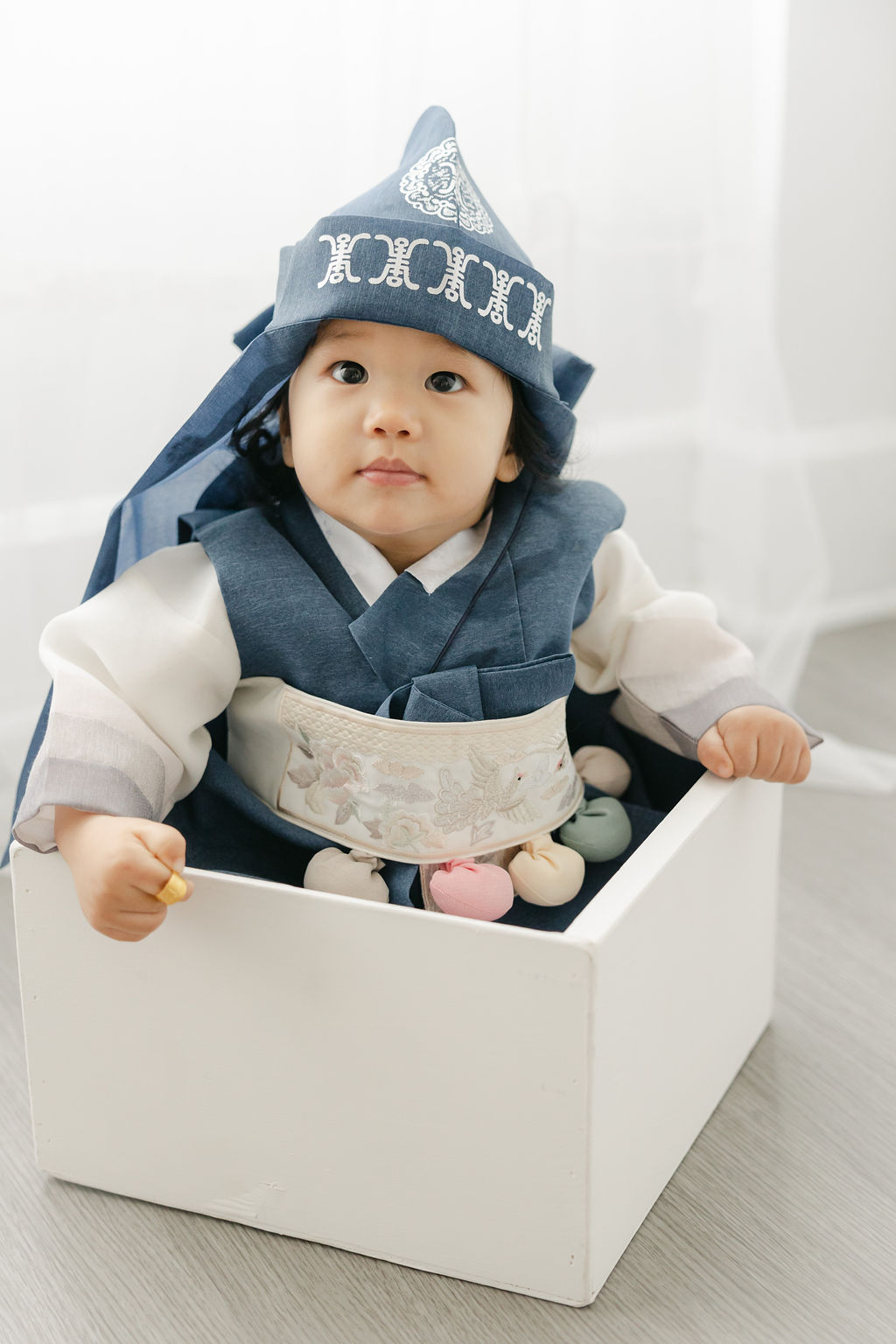 young boy in a blue hanbok sits in a white wooden box