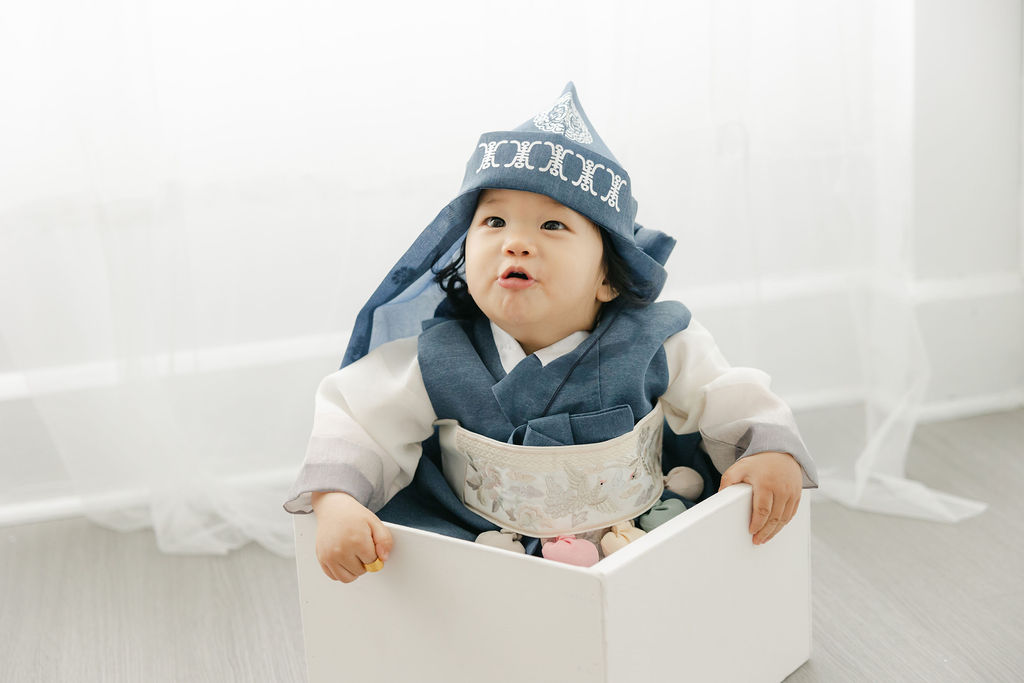 Toddler boy in a samurai outfit sits in a white wooden box in a studio hey little diddle