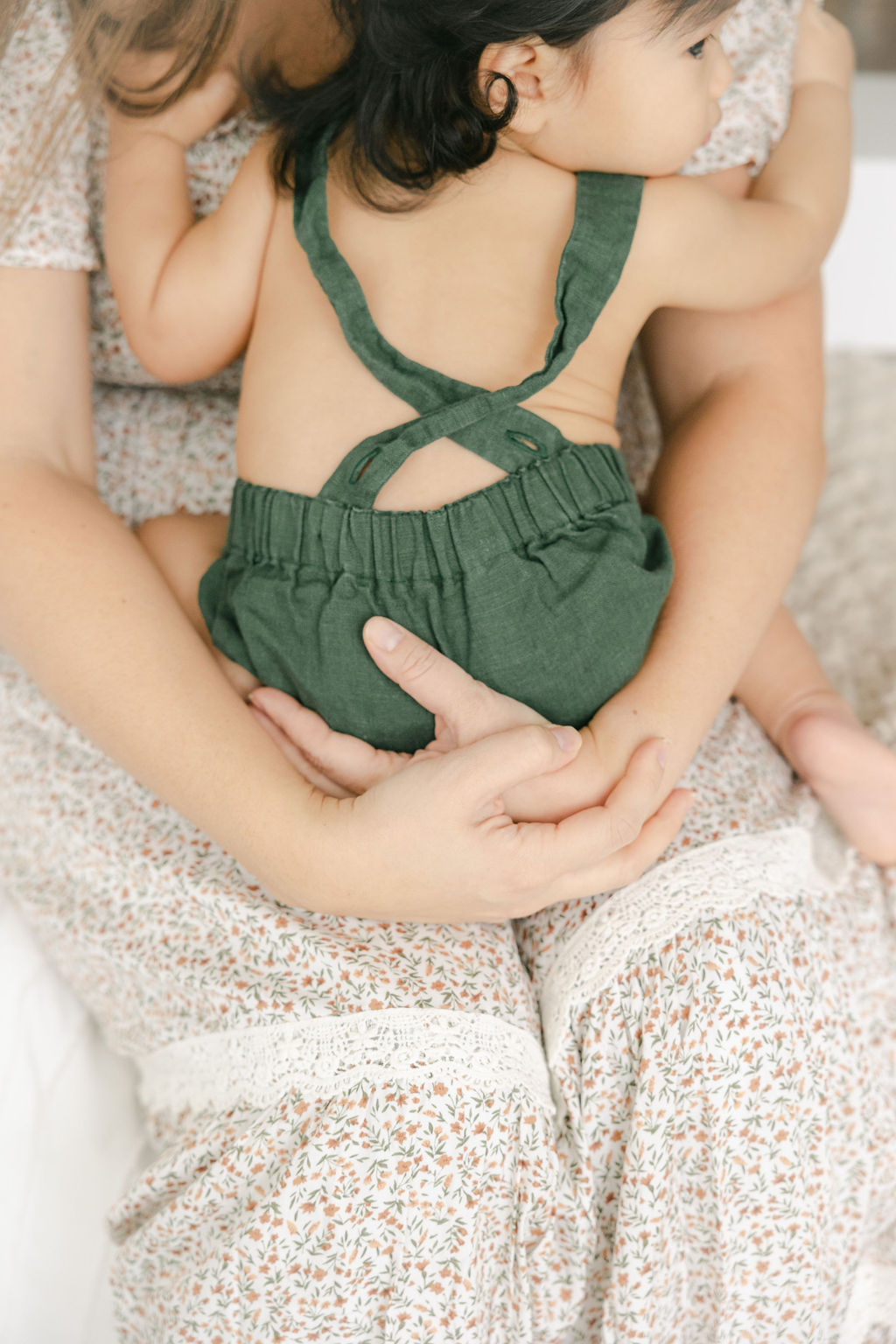 A toddler in green overalls sits in the lap of mom in a studio lil bloomers noblesville
