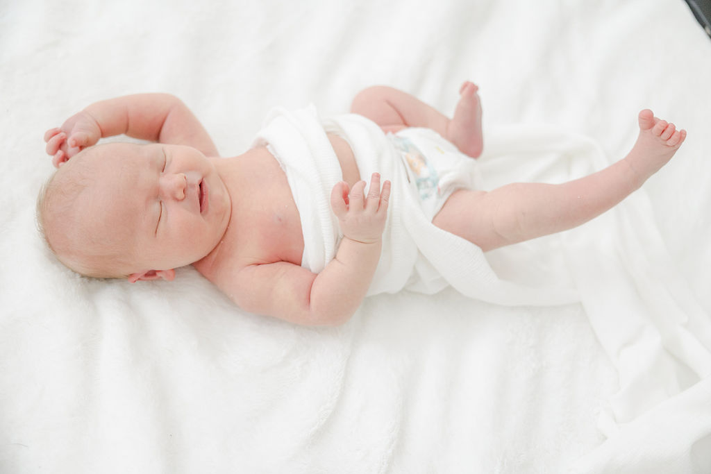 Newborn baby stretches leg out while laying on a white bed