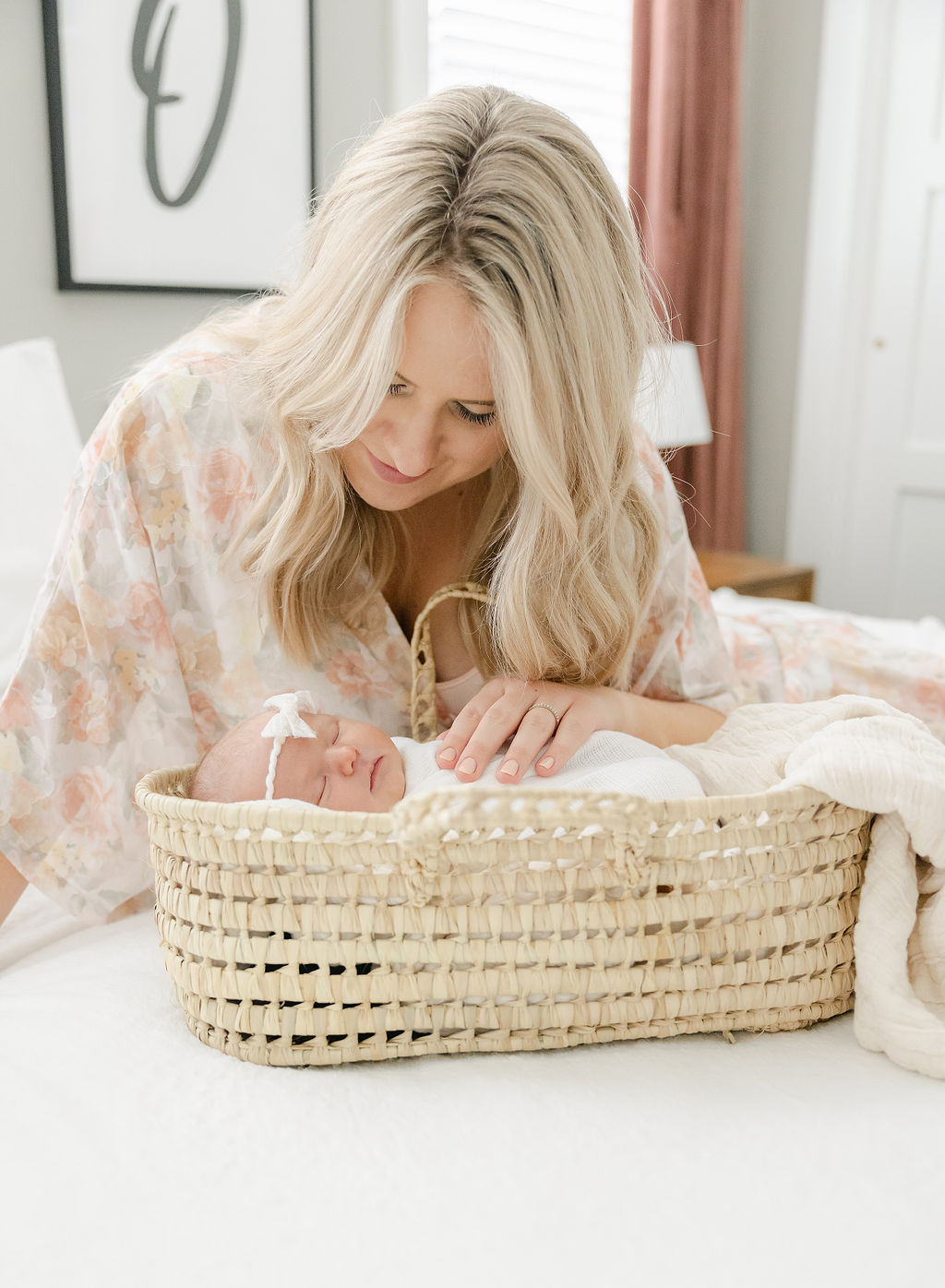 Mother looks over her newborn baby sleeping in a woven basket on a bed photographer in Indianapolis