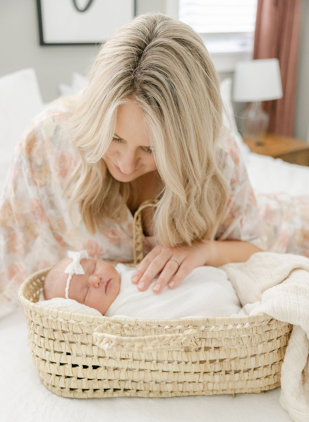 A newborn baby sleeps in a woven basket bed while mother leans over the top looking down on her indianapolis pediatricians