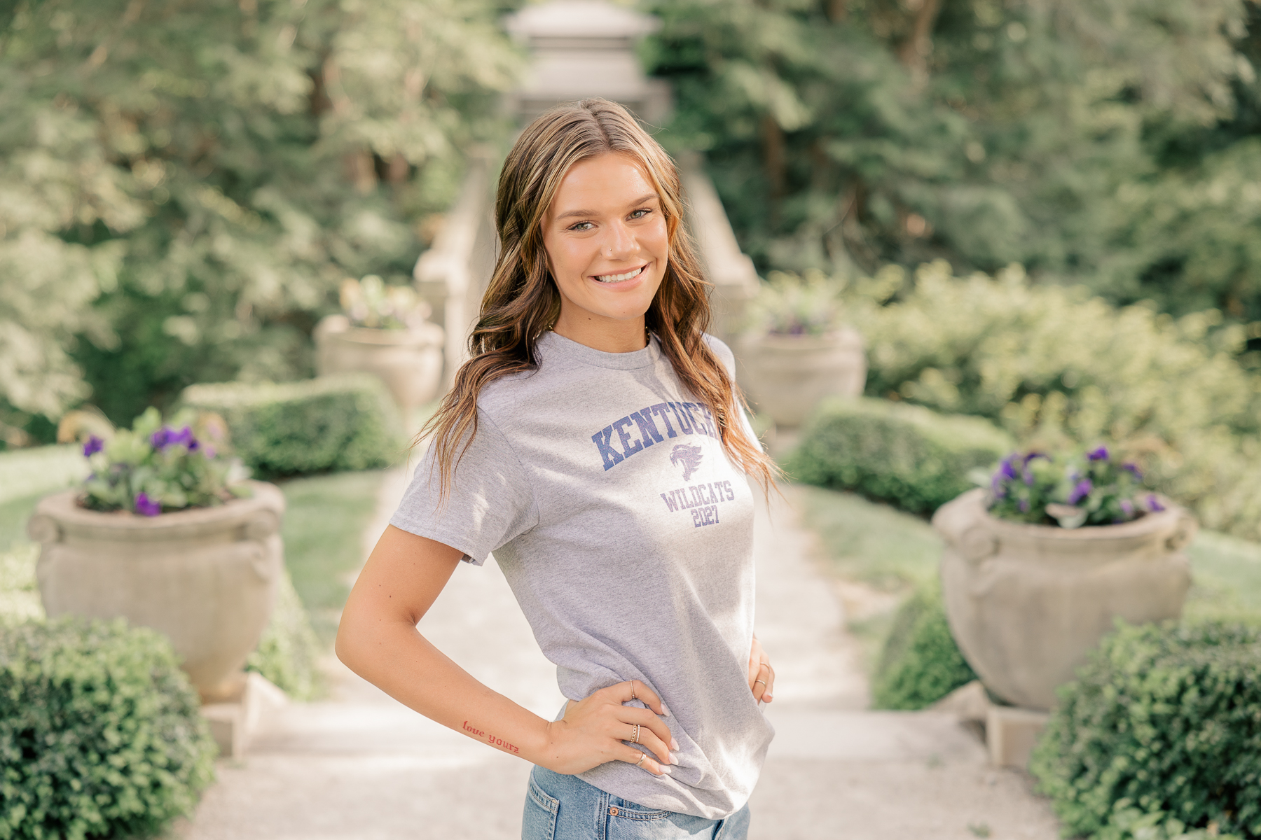 girl in a kentucky university shirt and jeans smiles at Newfields, Indianapolis Senior Pictures