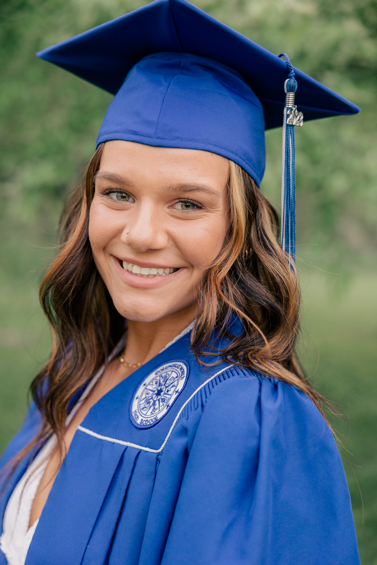 girl in blue graduation cap and gown smiles at Newfields, Indianapolis Senior Photographer