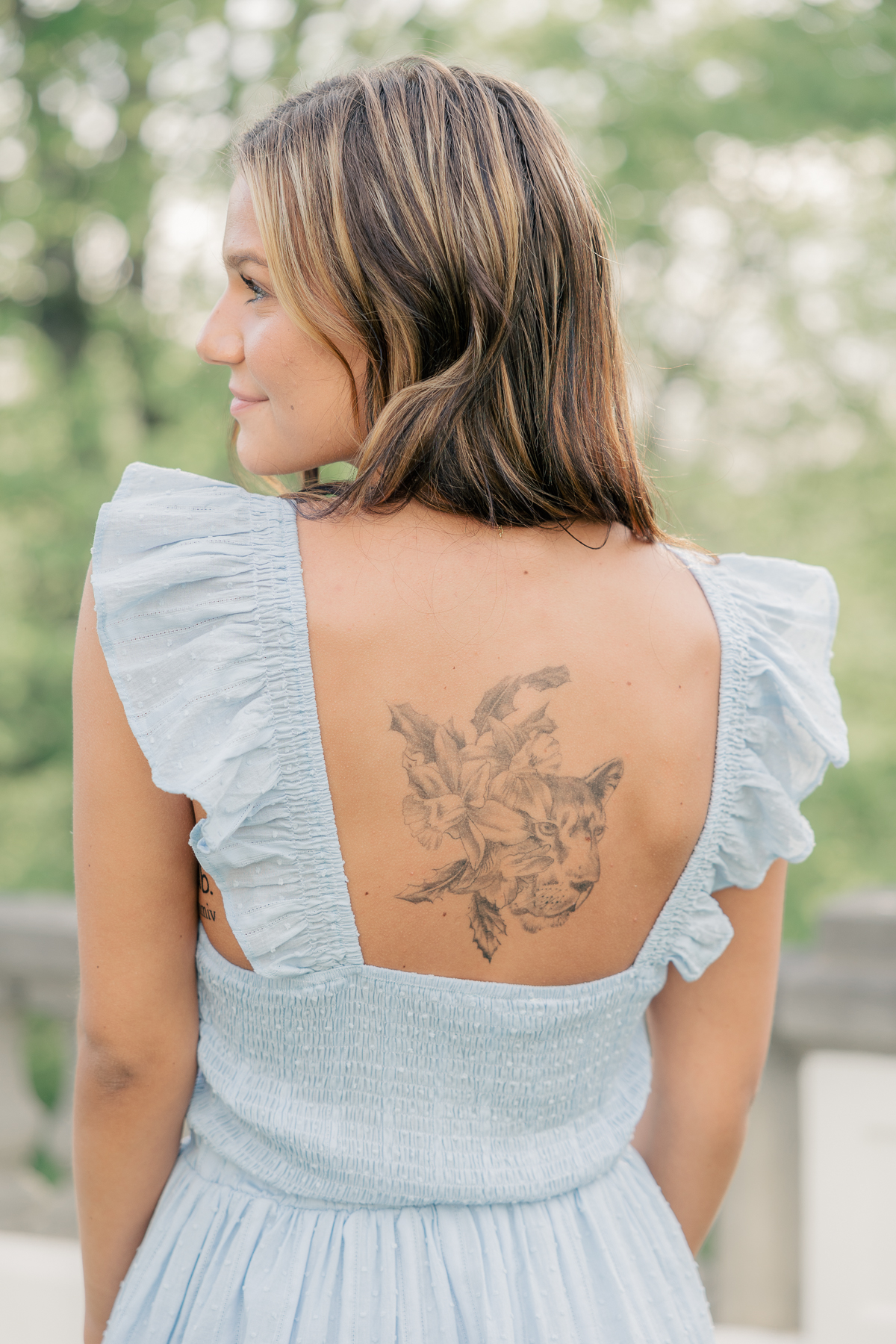 girl in a short blue dress shows memorial tattoo at the Lily House at Newfields, Indianapolis Senior Pictures