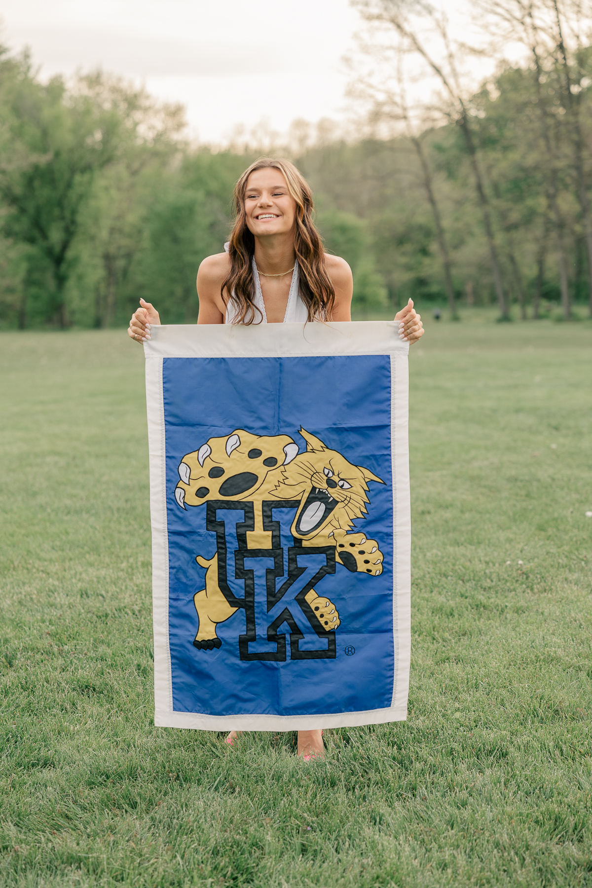 girl holds a kentucky university flag and smiles at Newfields, Indianapolis Senior Pictures