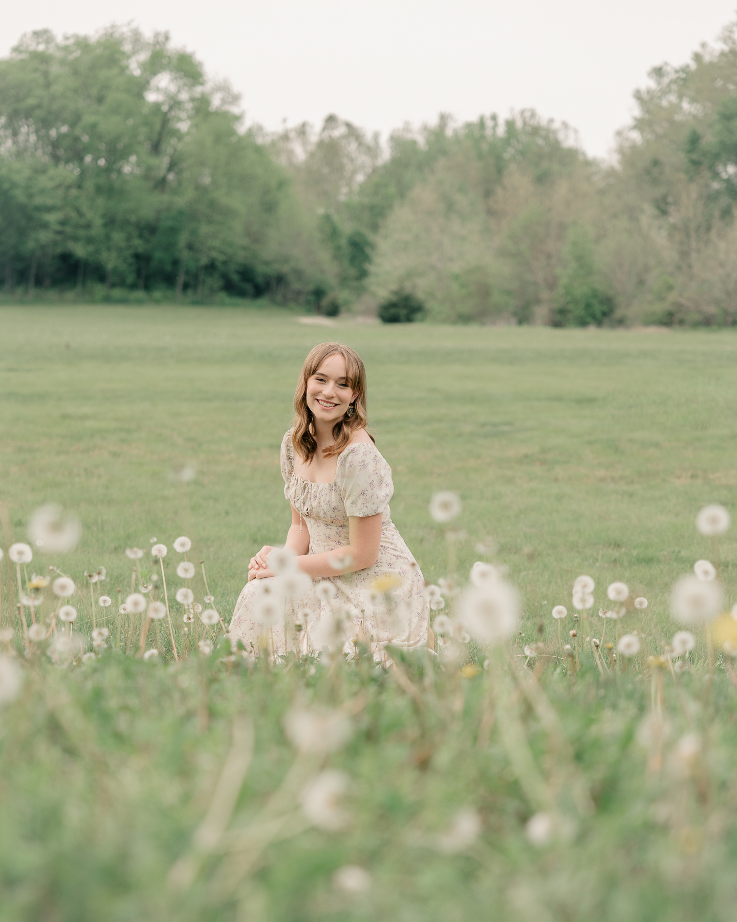 girl in long cream floral dress sits in a field of dandelions, Plainfield senior photography