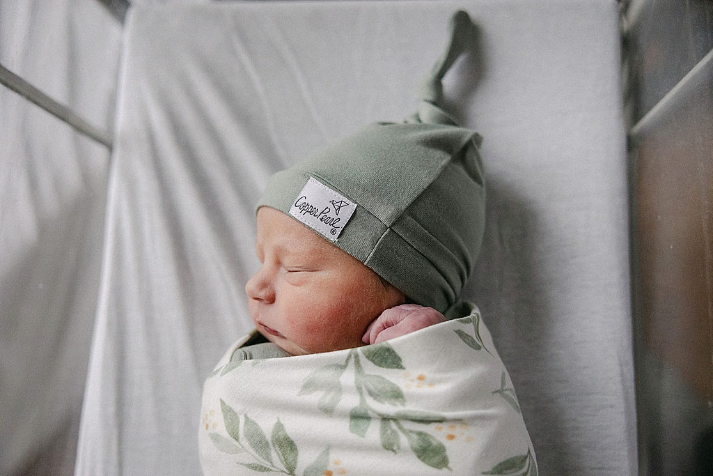 A newborn baby sleeps in a floral swaddle and matching green sleep cap carmel pediatricians
