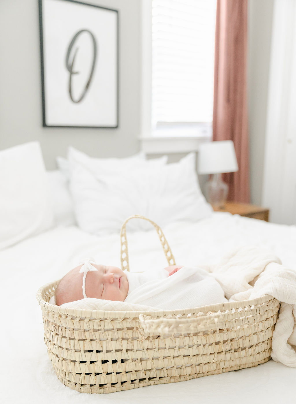 A newborn baby sleeps in a white blanket in a woven basket on a bed