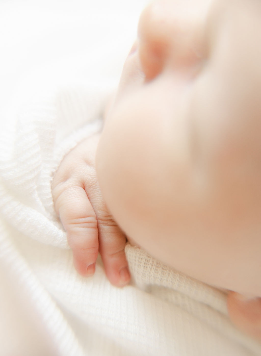 Details of a sleeping newborn baby with hand poking out of swaddle