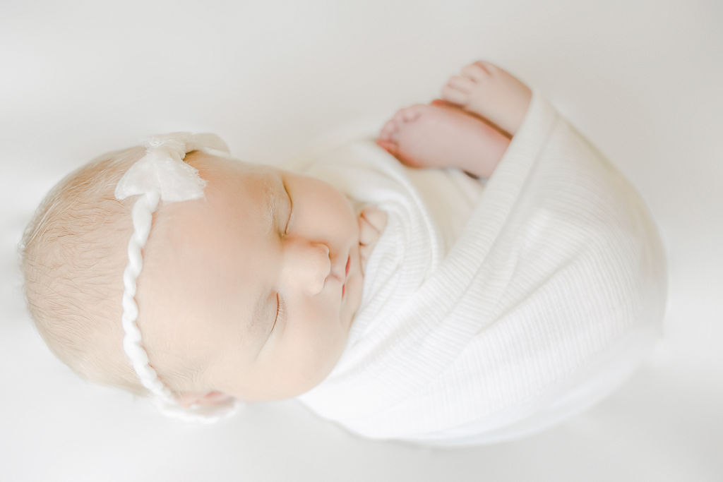 A newborn baby sleeps with toes sticking out of white swaddle indy night nanny