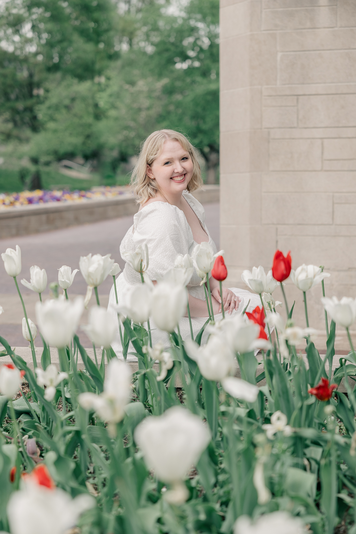 Senior photography session at IU Bloomington, woman in white dress sits by white and red tulip flowers