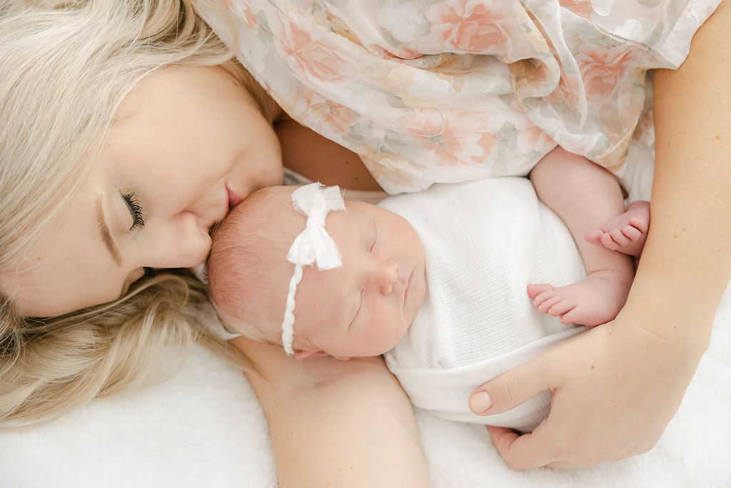 A new mother cuddles and kisses her sleeping newborn baby