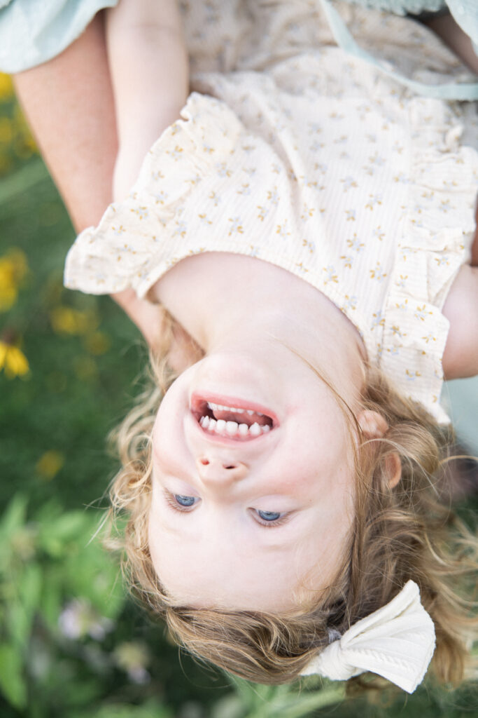 Toddler girl in cream floral dress giggles as she is being held upside down by mom