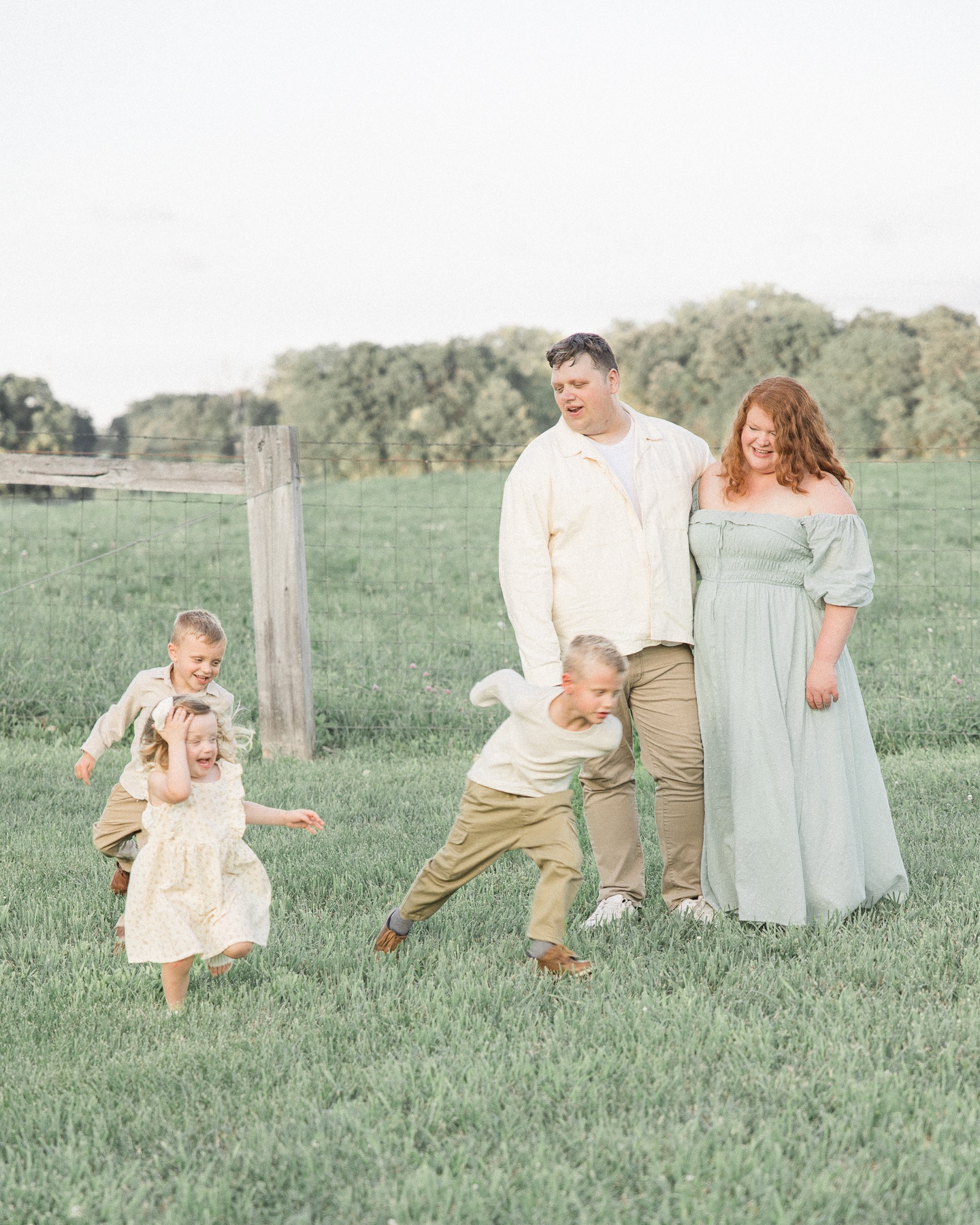 Mother and father stand together as their three young children run around them in a grassy field at Trader's Point creamery indianapolis baby shower venues