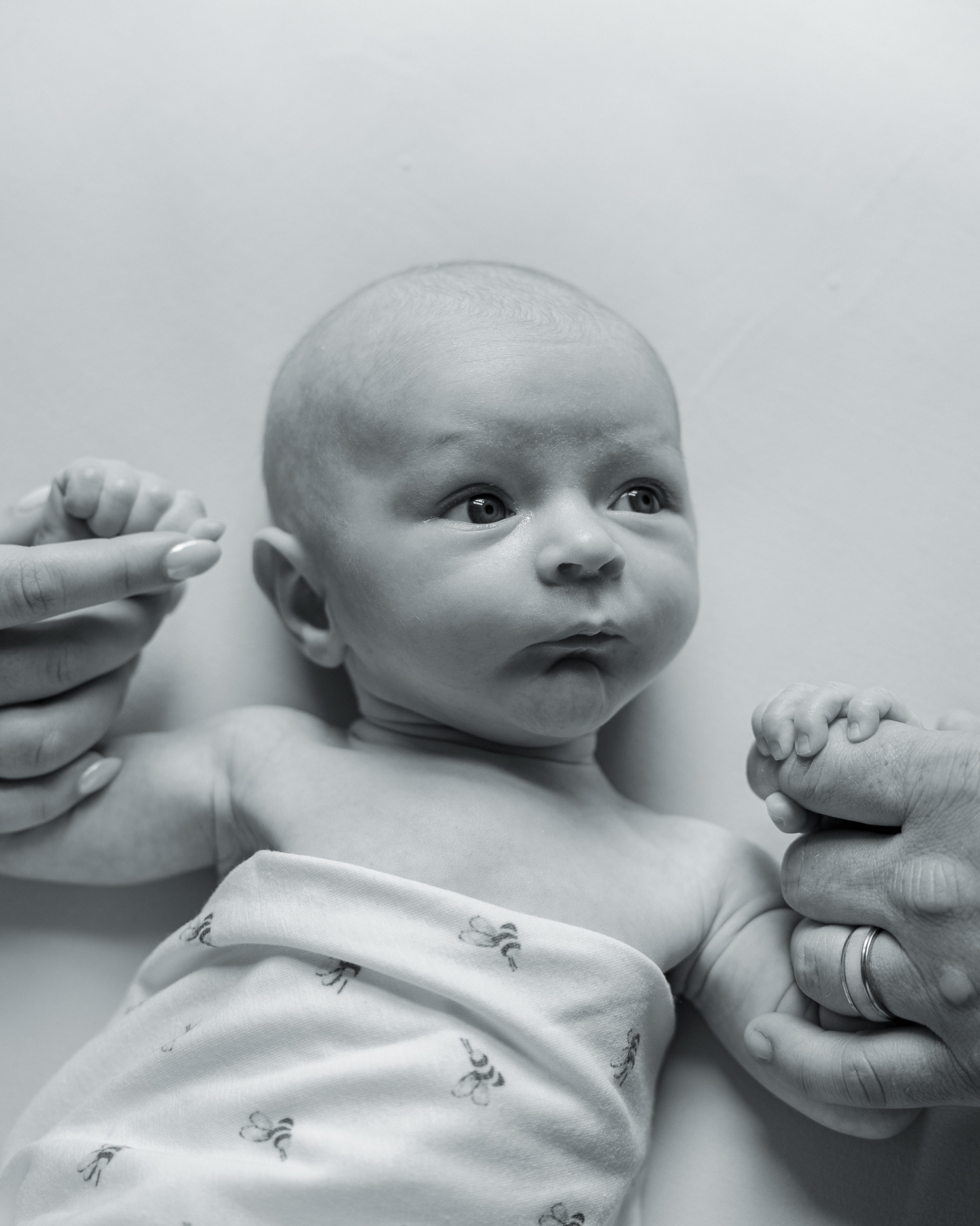 black and white image of a newborn baby looking at his parents as they hold his hands, lifestyle newborn photography