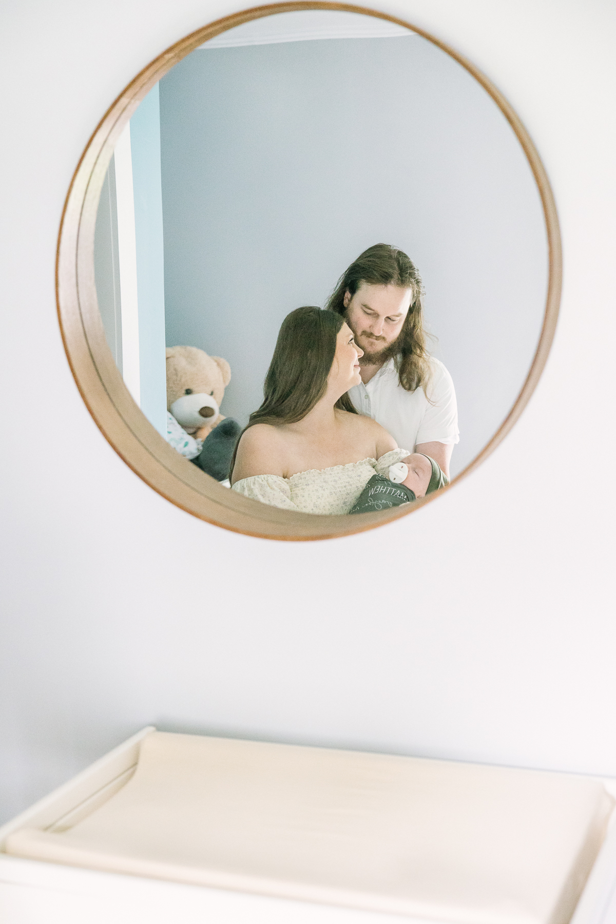 Mother holds her newborn son while looking at her husband in a nursery mirror, lifestyle newborn photography