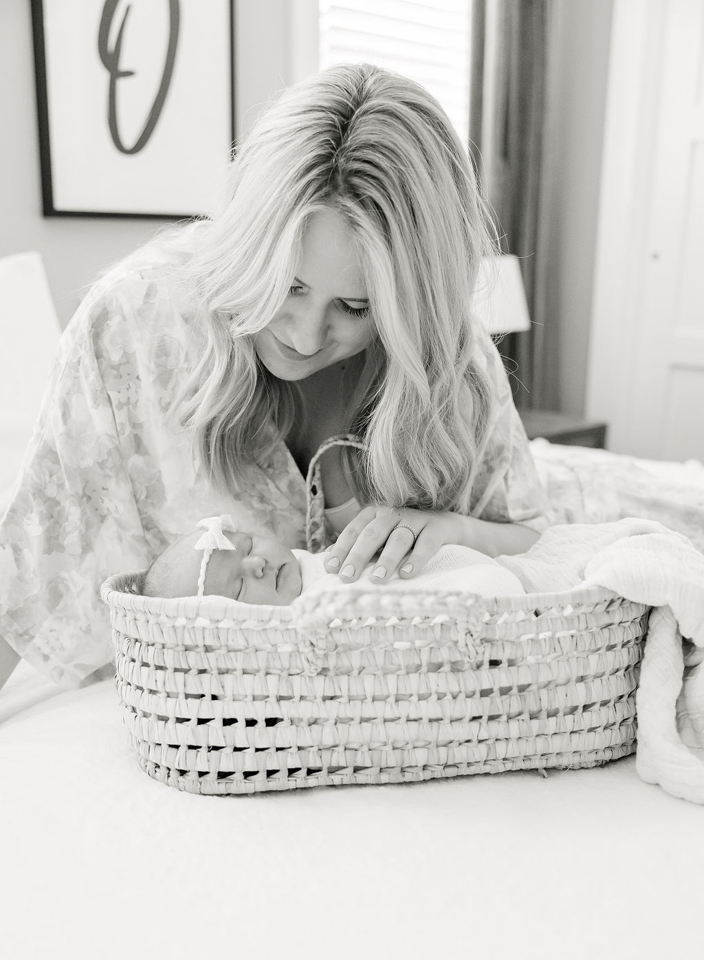 A new mother leans over and places her hand on her sleeping newborn baby in a woven basket nannies indianapolis