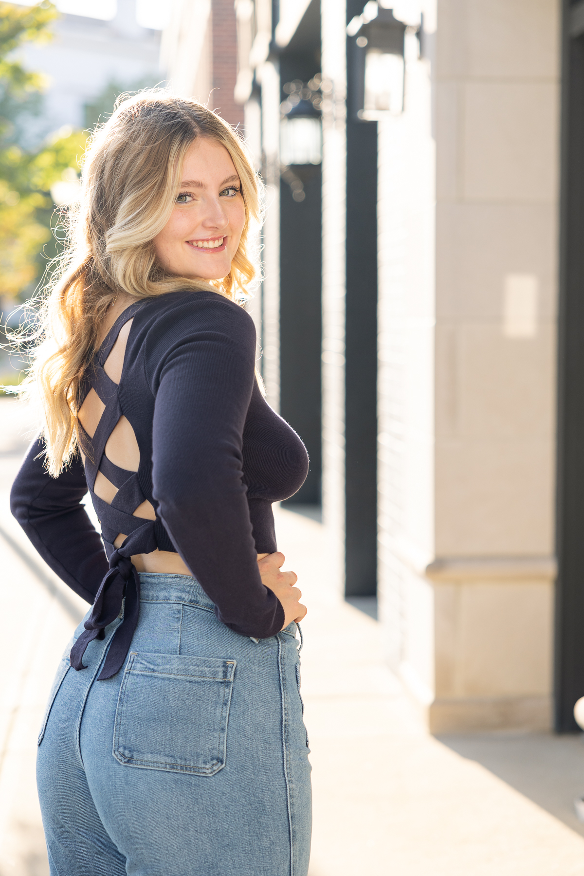 girl turns to look over her shoulder in a strapy top and jeans, Carmel senior pictures