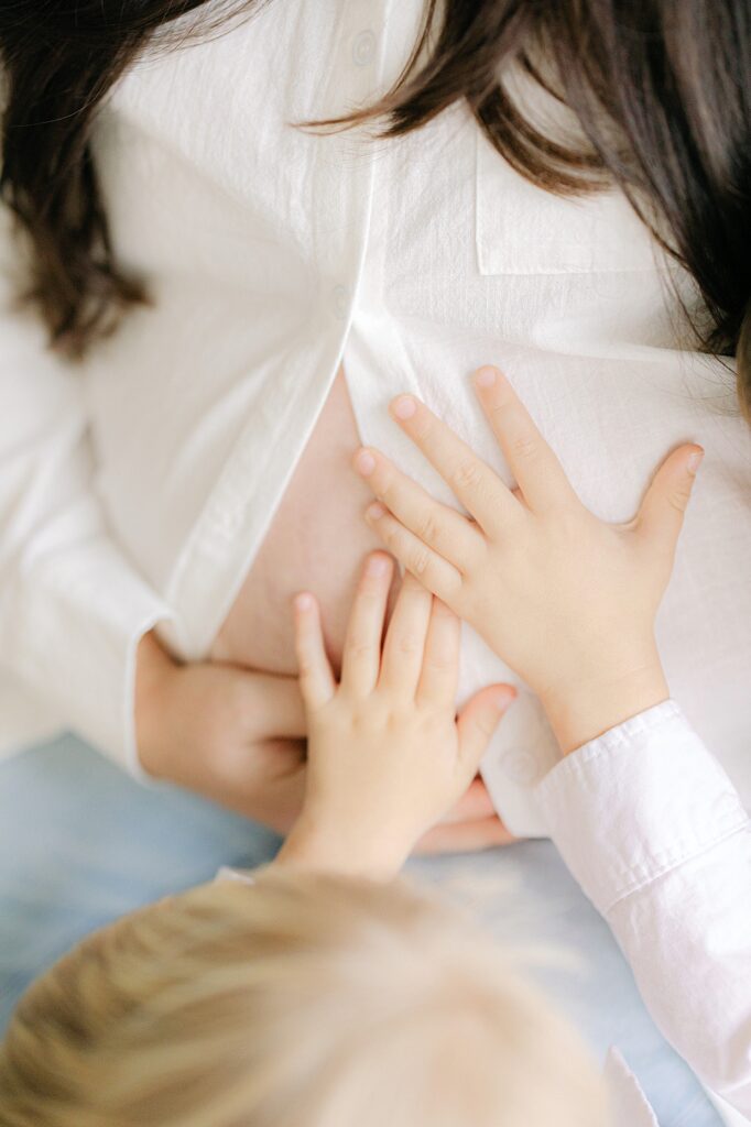 two brother's hands reach out to feel their baby brother kicking in their pregnant mother's belly during Family photography in Carmel