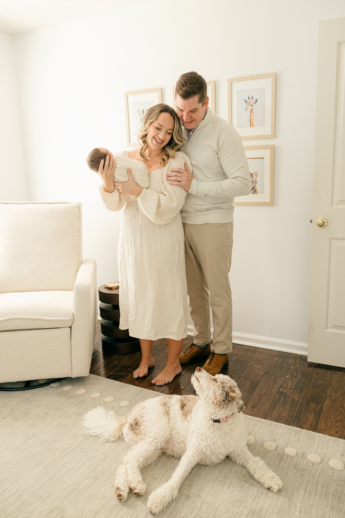 New mother and father holding their baby swaddled in cream in the nursery while smiling down at their dog, Indianapolis Photographer