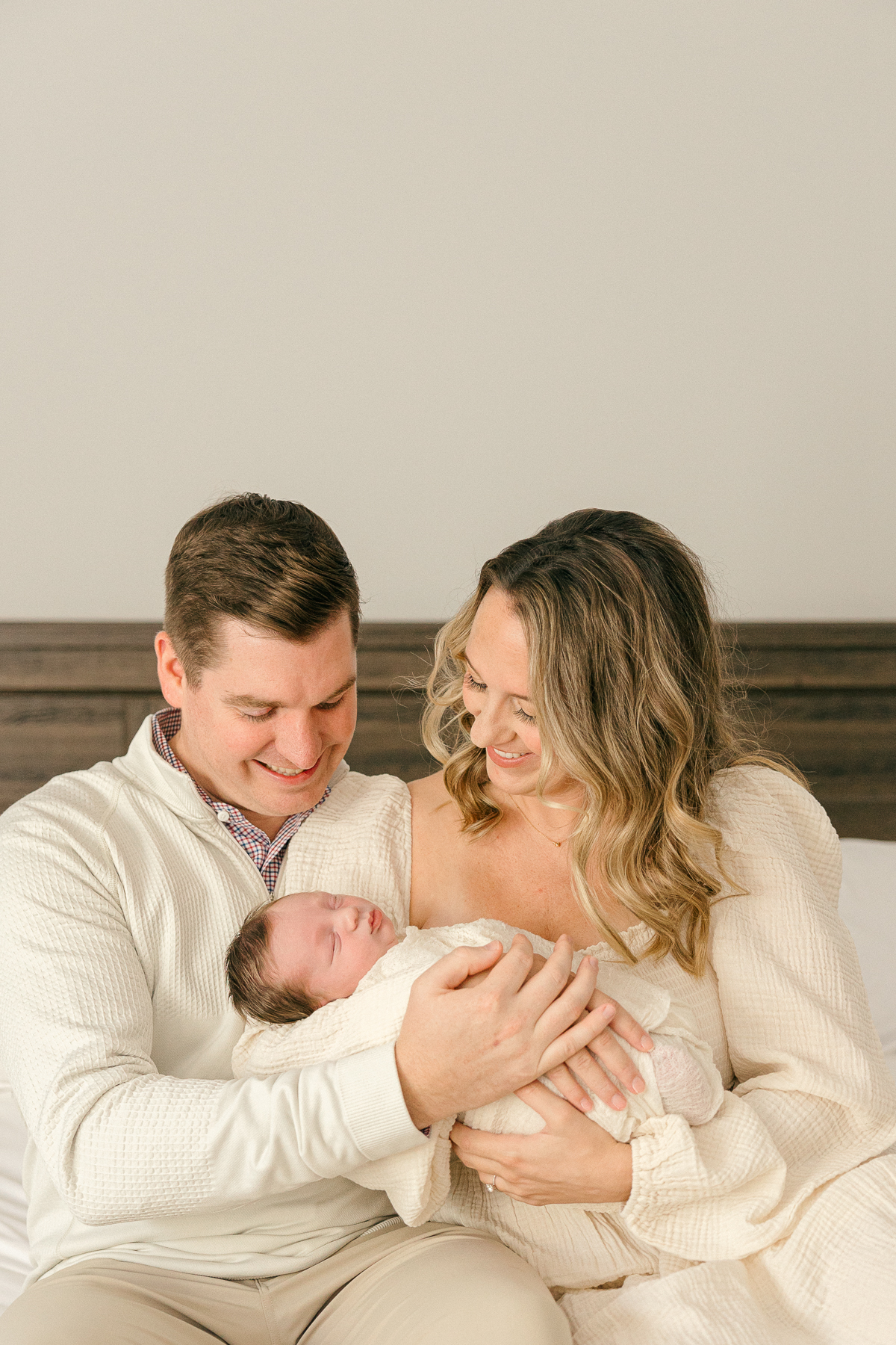 new parents sit on bad while holding newborn and looking at him lovingly, Indianapolis Photographer