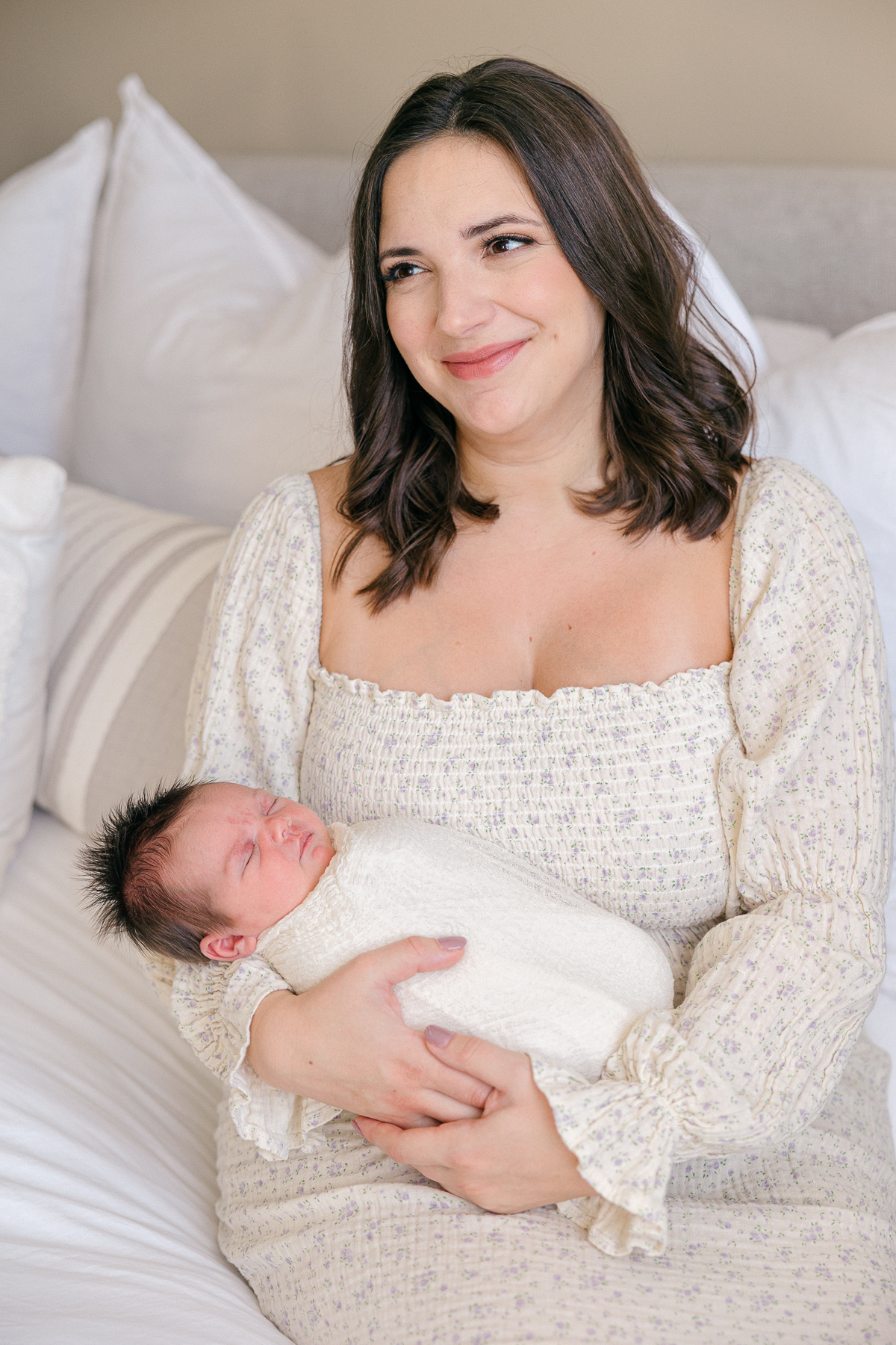 Mother in a cream and floral dress holds her baby girl swaddled with a cream blanket, Fishers Newborn Photographer
