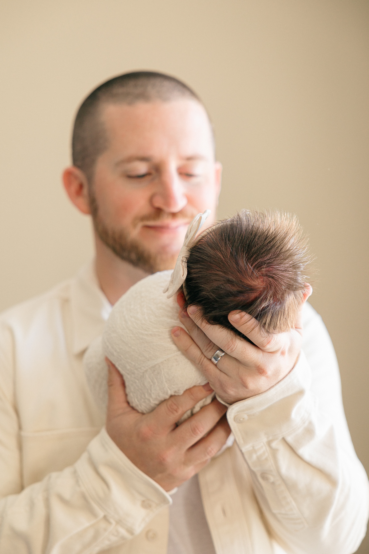 father smiles at his newborn daughter as he holds her in his hands, Fishers newborn photographer