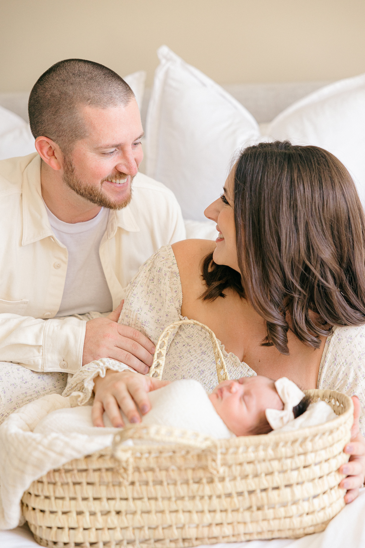 mother and father smile at each other while their newborn baby girl sleeps in a moses basket, Fishers newborn photographer