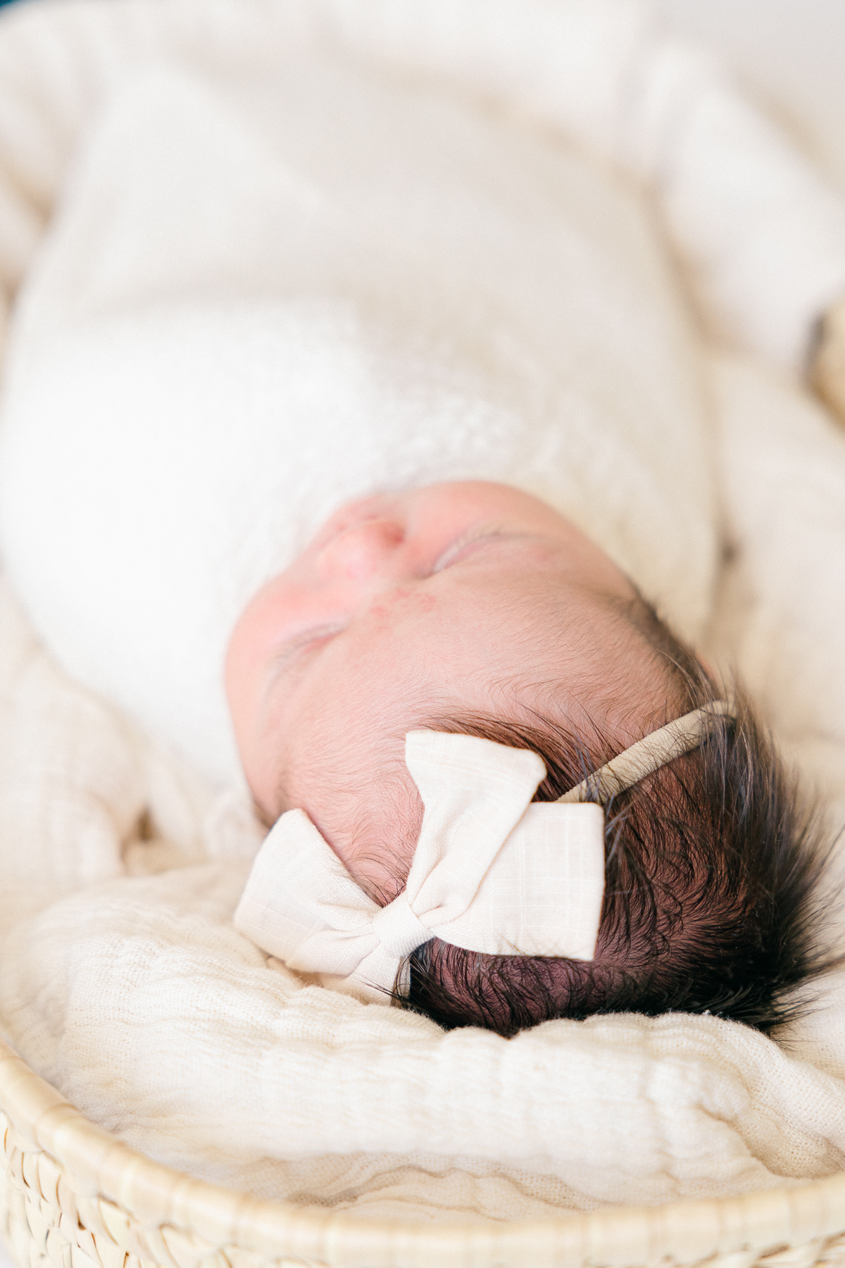 Baby girl swaddled in cream blanket with cream bow sleeps in a moses basket, Fishers Newborn Photographer