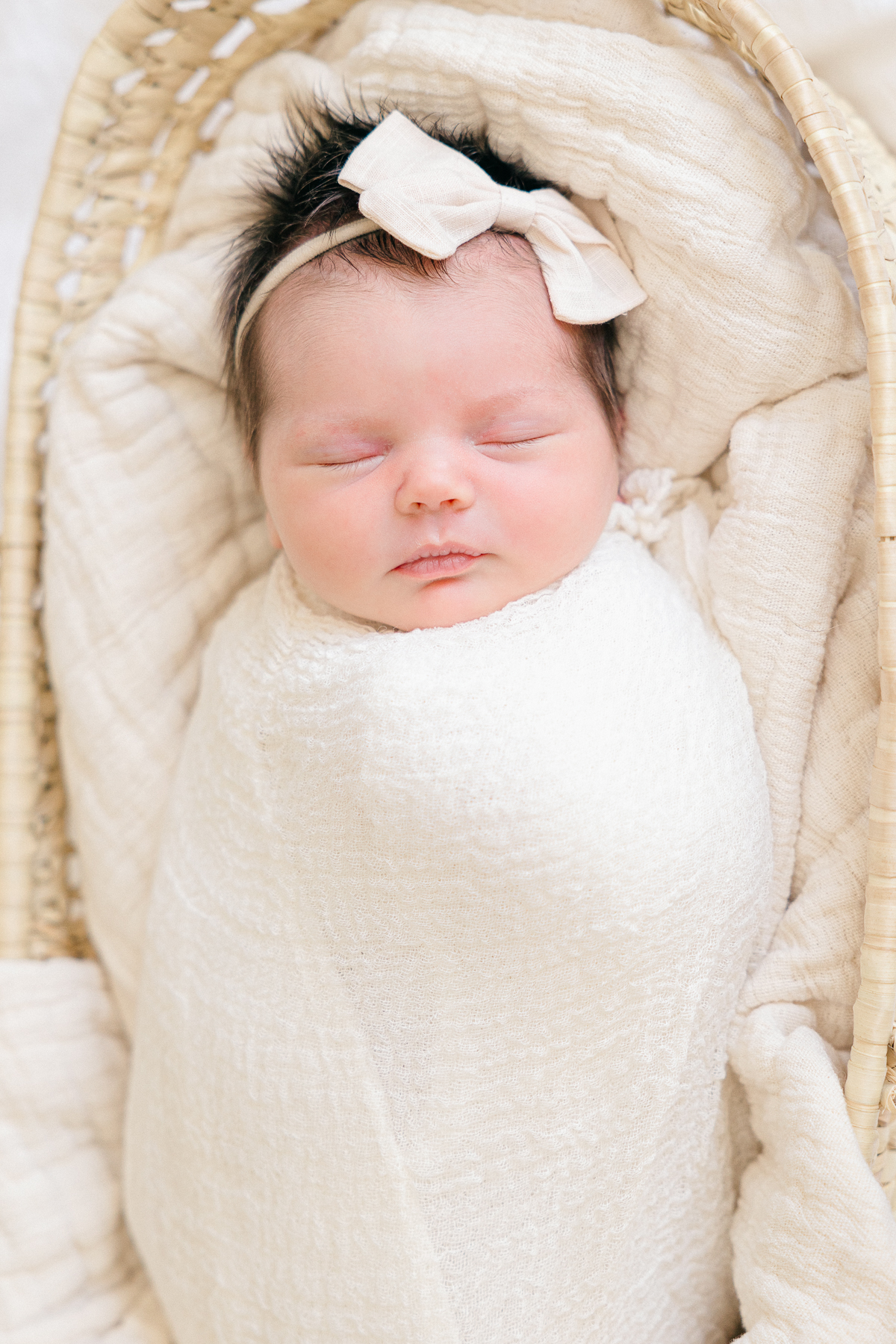 Baby girl swaddled in cream blanket with cream bow sleeps in a moses basket, Fishers Newborn Photographer