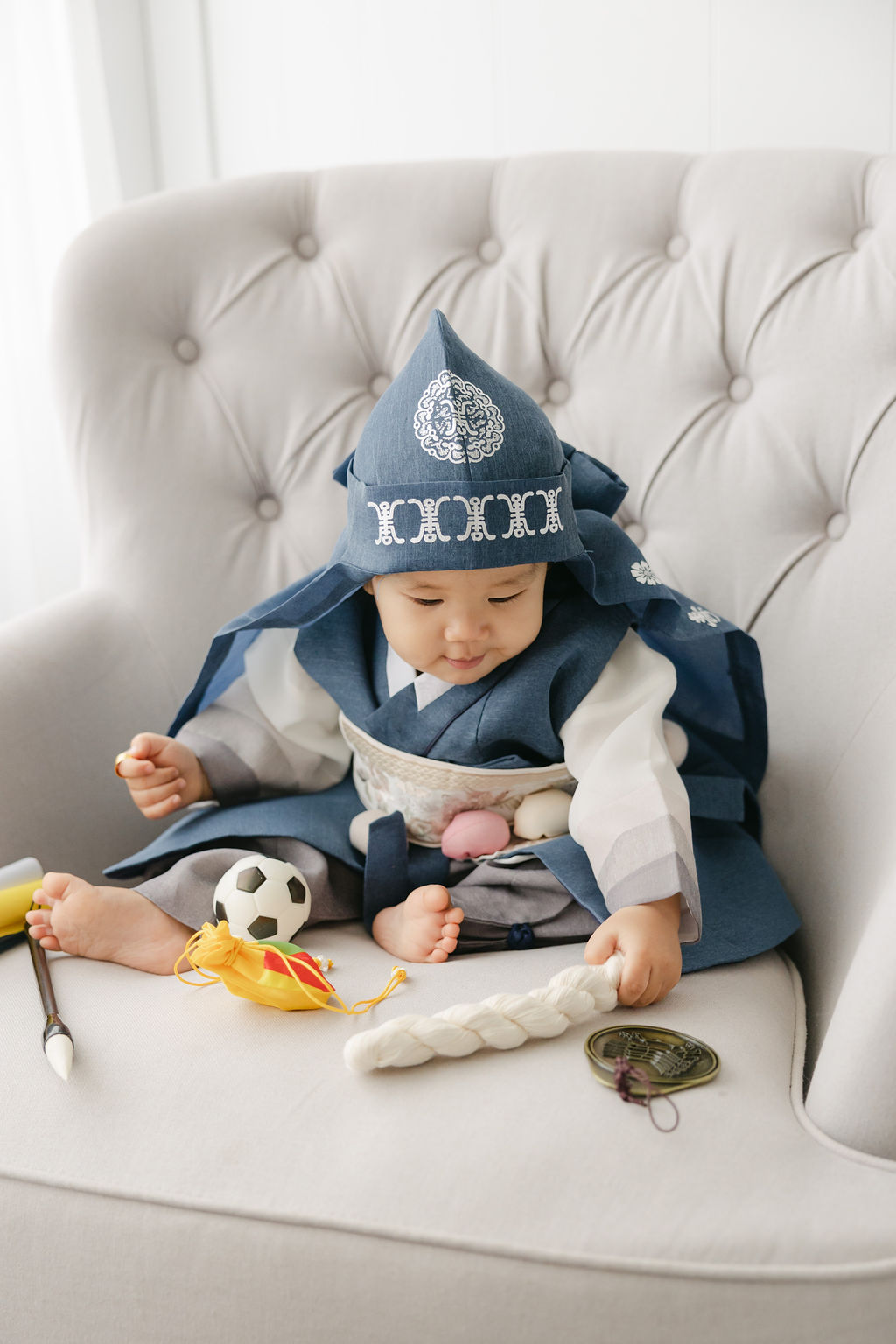 A young boy sits in a blue outfit surrounded by toys in a studio