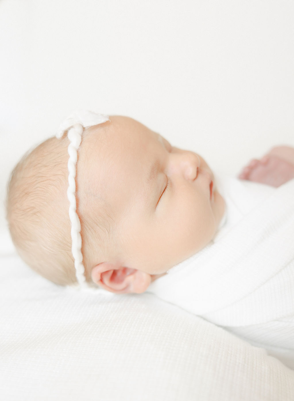 A newborn baby sleeps in a studio with a white bow from the birth hub