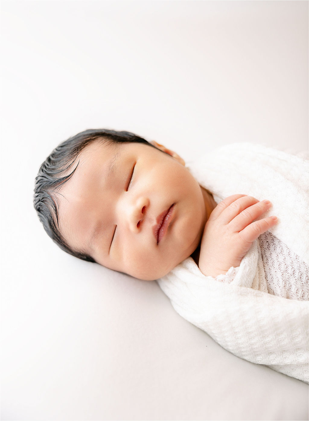 A newborn baby sleeps on a white bed in a studio