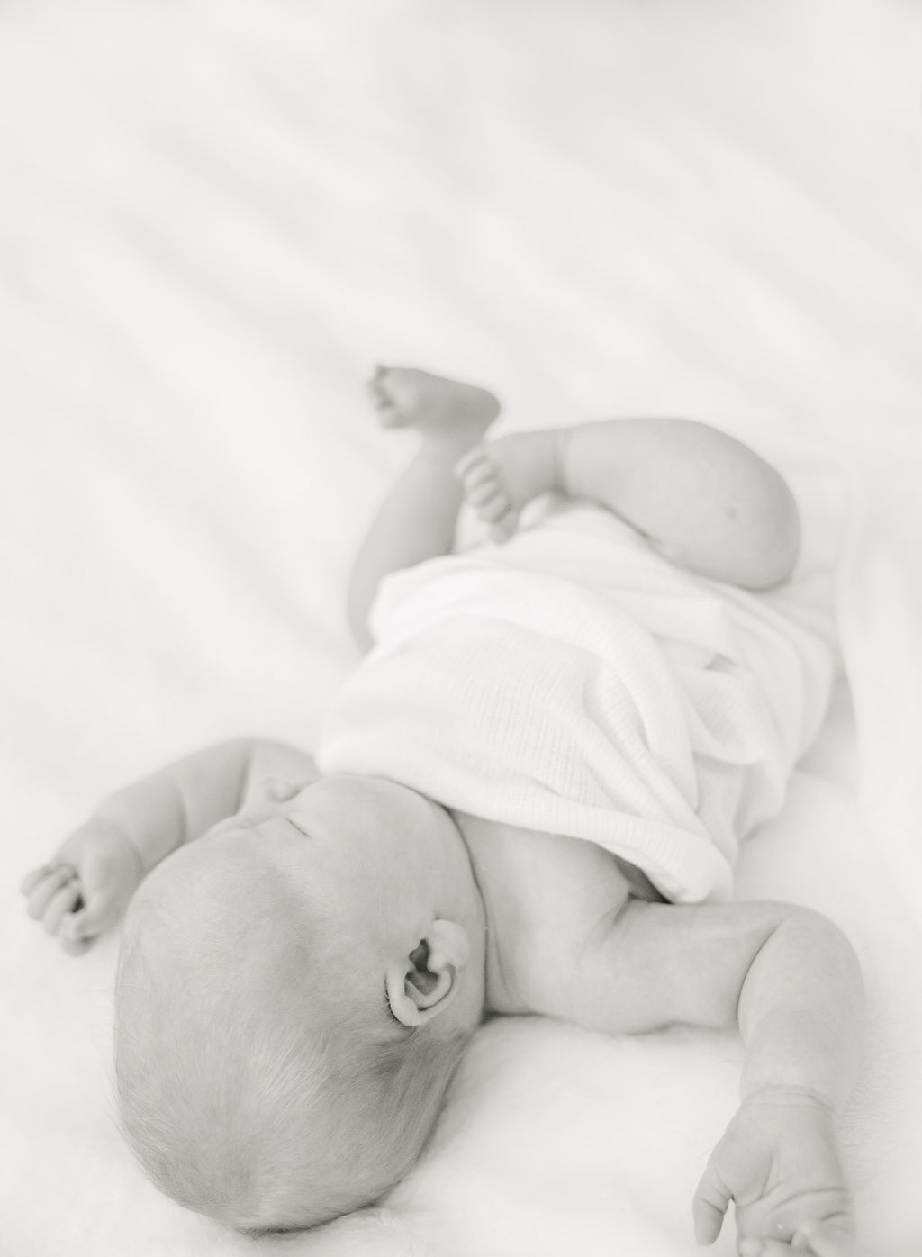 A newborn baby sleeps under a white blanket on a bed after meeting a lactation consultant indianapolis