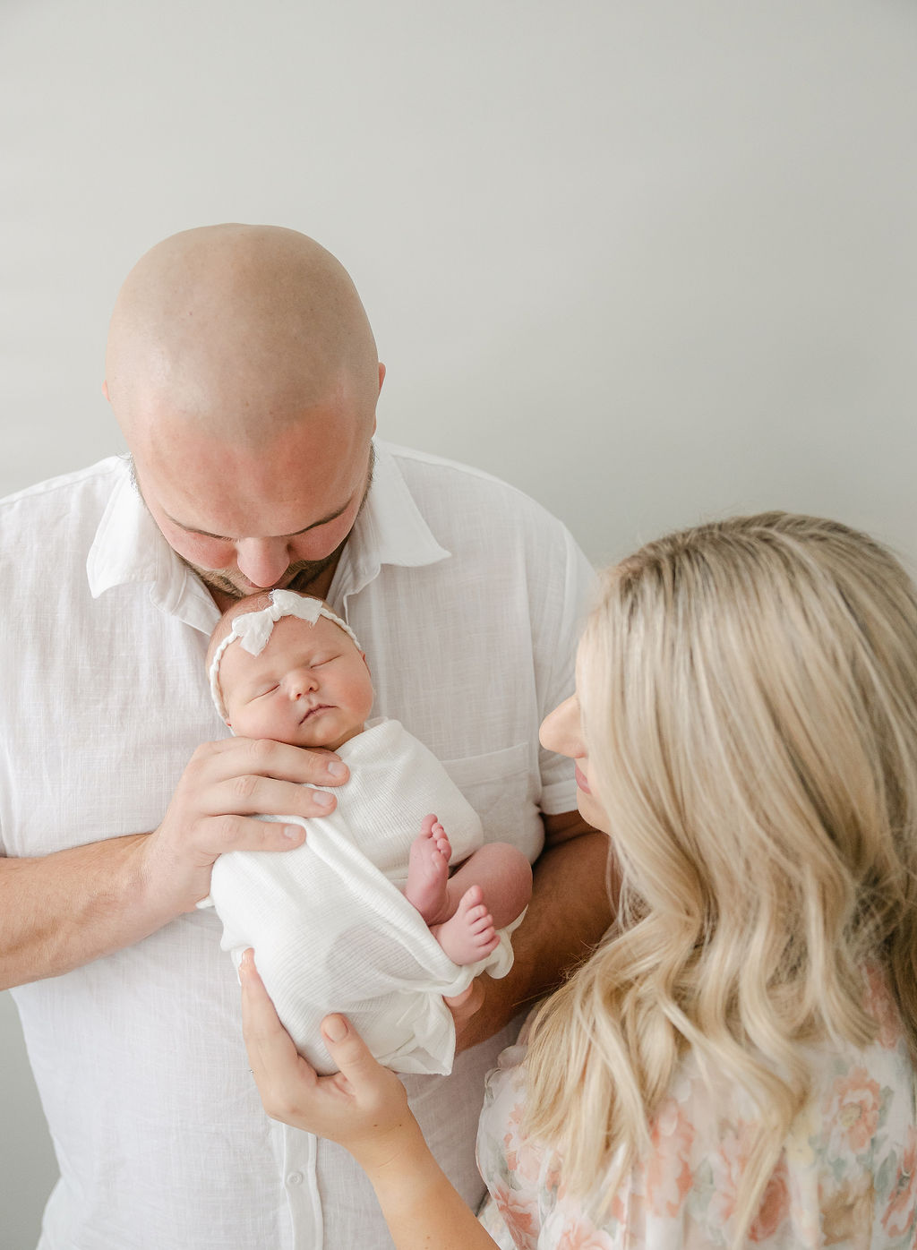 A father kisses the head of his sleeping newborn daughter in his hands while standing in a studio before visiting zionsville pediatric dentistry