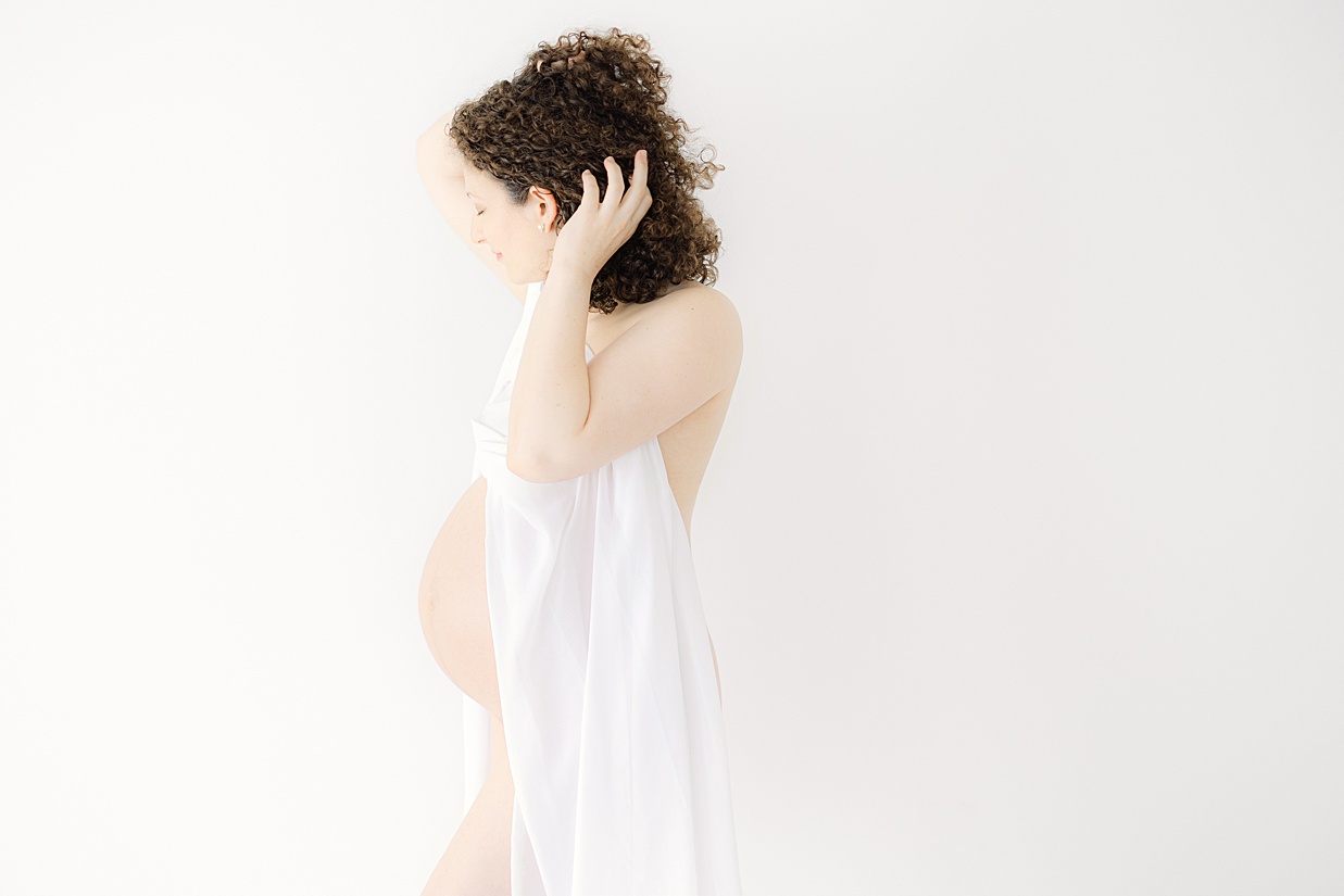 A pregnant mother runs her hands through her hair with her baby bump exposed Indianapolis baby shower venues