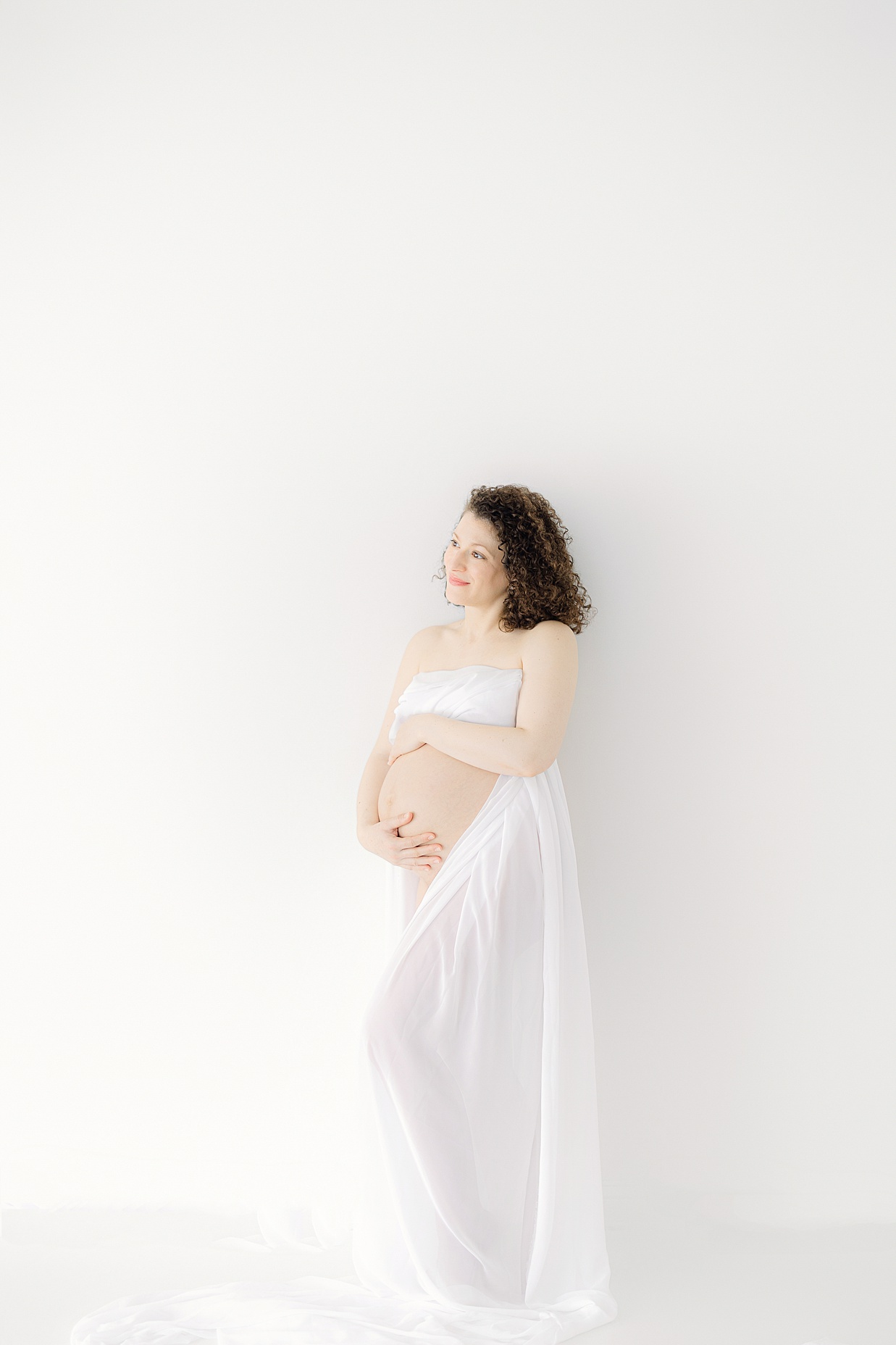 Pregnant mother holds her bare baby belly wrapped in a white sheet thanks to obgyn carmel indiana