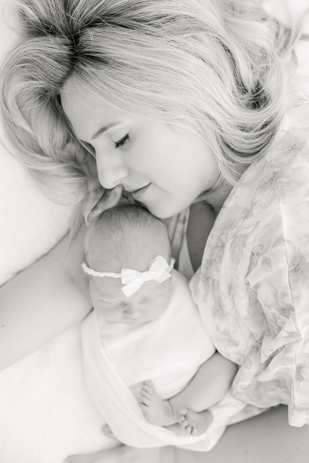 A mother snuggles with her sleeping newborn baby in a studio on a bed after meeting au pair indianapolis