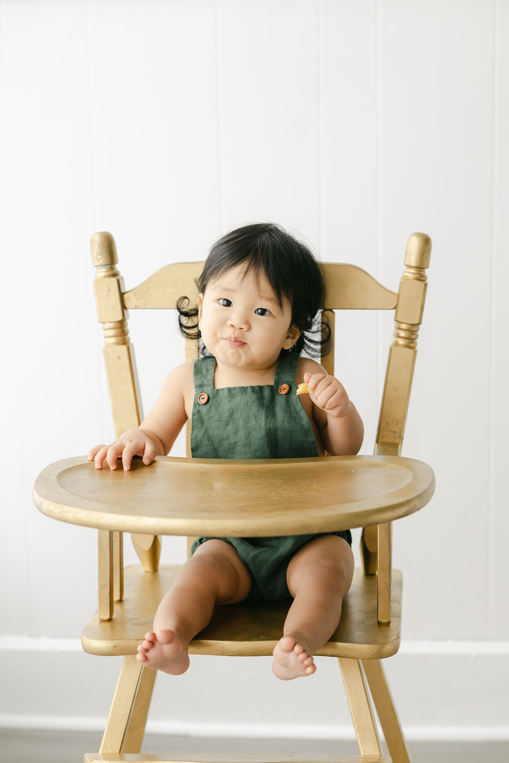 A young toddler boy sits in a wooden high chair in green overalls after meeting carmel pediatric dentistry