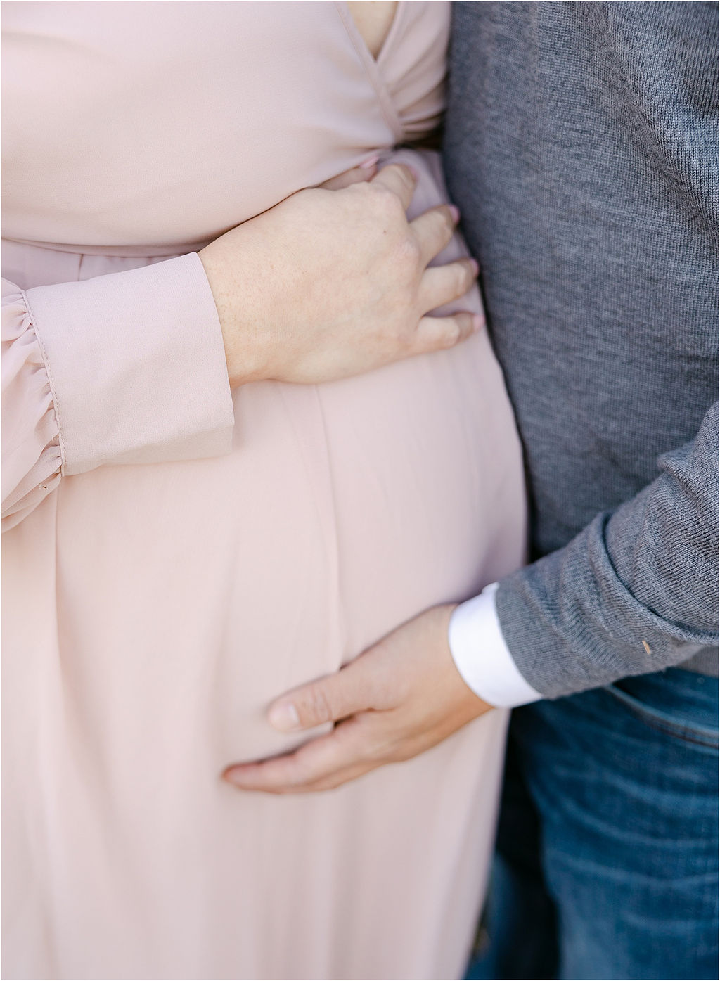 Details of expecting parents standing close and holding the bump