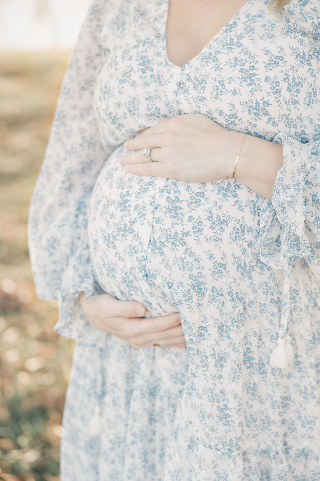 Details of a mother to be in a blue floral dress holding her bump in a field after visiting serene midwifery