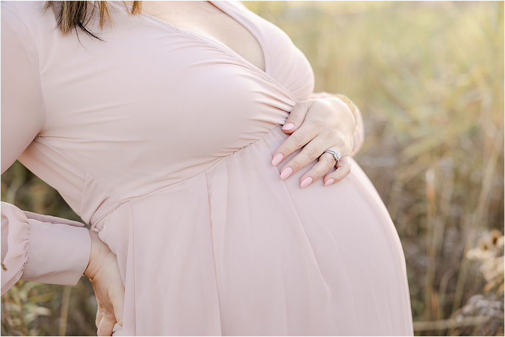 Details of a mother to be holding her bump in a pink maternity dress